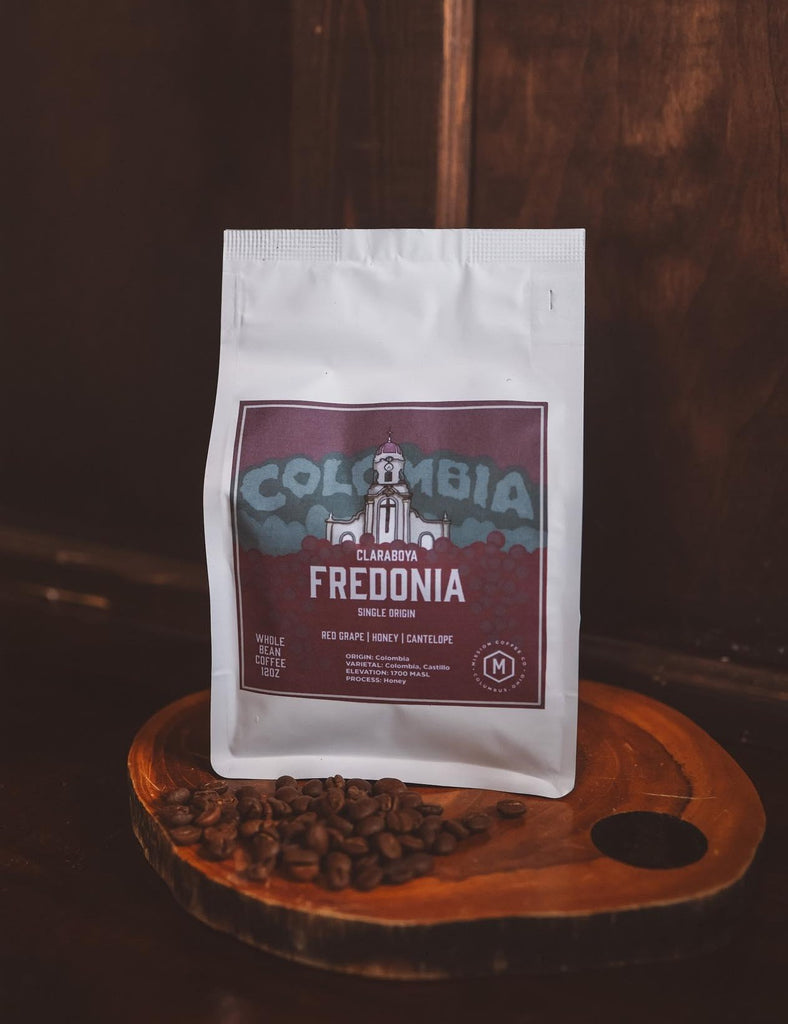 Local coffee roasted in Columbus Ohio.  Colombian Coffee, Single Origin, honey processed roast.  White coffee bag with plum colored label on wood background with loose coffee beans.